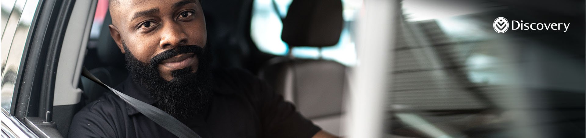 Discovery Promotion Banner: A bearded man sitting in a car smiling.